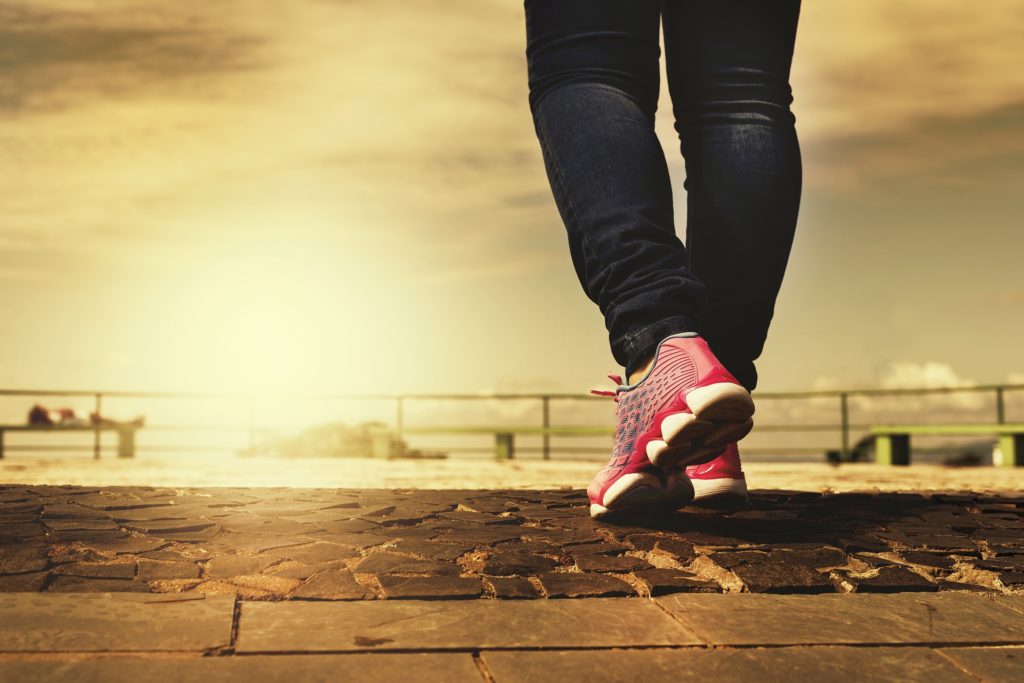 nervous system stuck in fight or flight, image of Sepia-toned image showing a person’s feet as they walk along cobble stone wearing pink tennis shoes—a representation of mindful walking for restoring a nervous system stuck in fight or flight.
