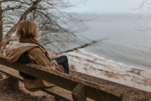 A fatigued woman looking out at a cold, calm lake. 