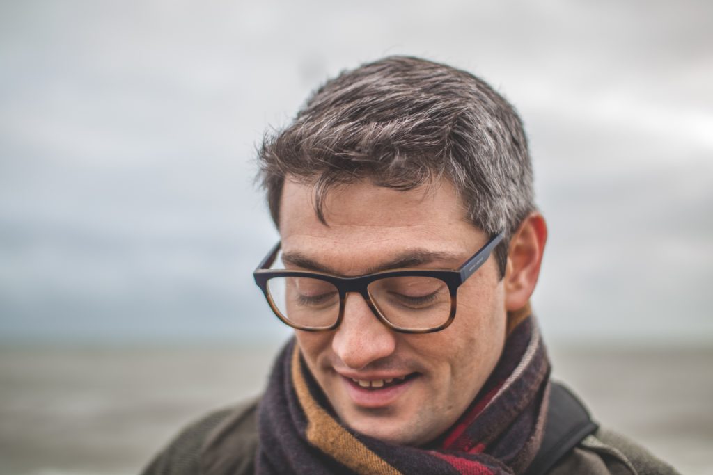 belly fat and ed, Up-close photo of a man who appears to be in his 40s, standing outside in overcast weather, wearing a scarf and glasses, with a slight smile on his face—portraying the joy of treating excess belly fat and ED.