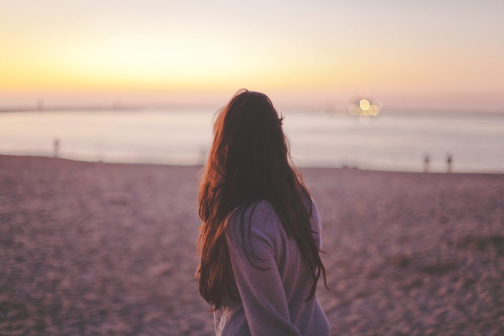 Woman walking along a beach at sunset.