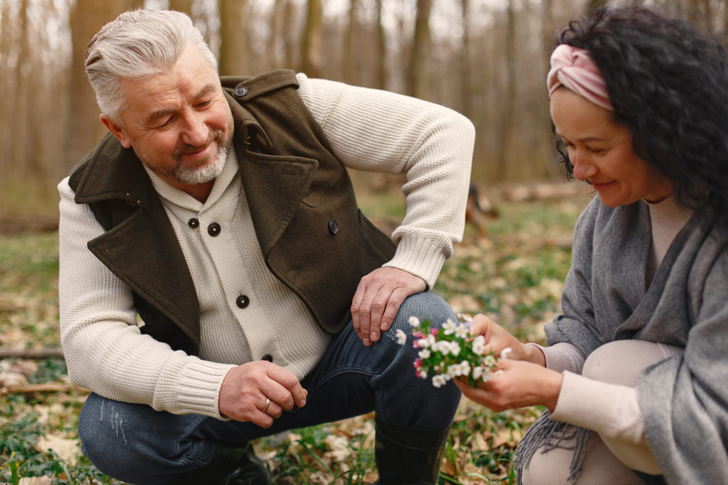 ldn benefits, image of two people who appear to be in their 50s or 60s, crouched down side by side in a wooded area, both smiling and looking at a bouquet of wildflowers that one of them is holding—representing the joy, pain relief, and renewed activity that LDN benefits can bring.