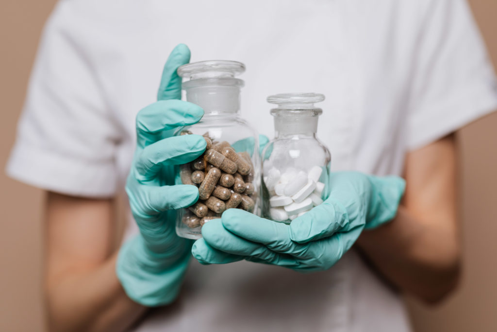 ldn benefits, image of a person’s gloved hands holding two glass pill bottles, one filled with brown capsules and the other with white tablets—representing the varying uses of naltrexone and LDN benefits.