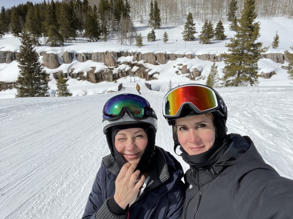 root cause of hair loss, Photo of Dr. Natasha Thomas and a friend, standing side by side at the top of a ski hill—both smiling and looking at the camera as they take a selfie—portraying the thing that led Dr. Thomas to discover the root cause of hair loss for herself.