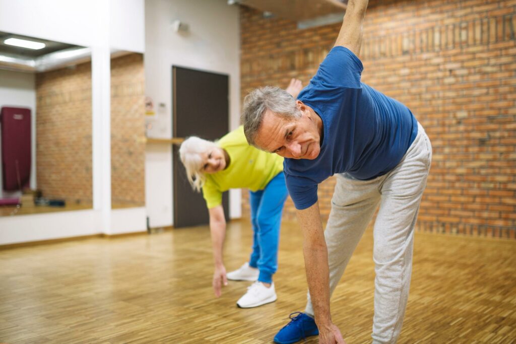 Cardio and Strength Training, old white couple stretches in a fitness studio with brick walls
